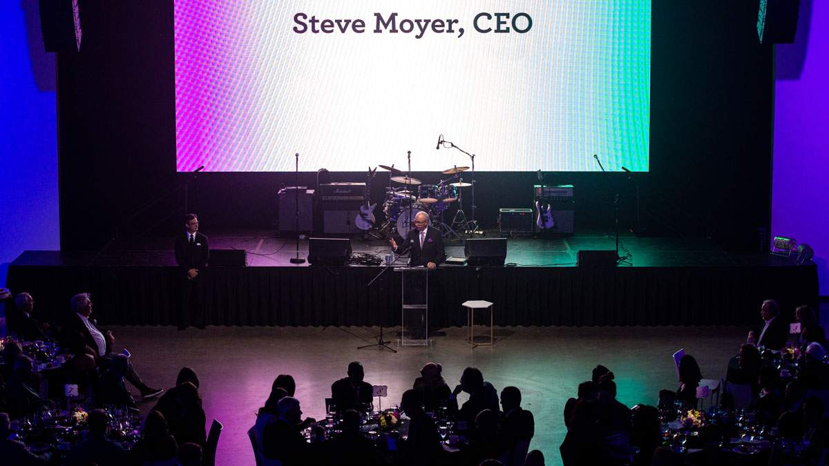 A CEO speaks to his employees at an elegant annual company meeting helf in a luxurious event setting.