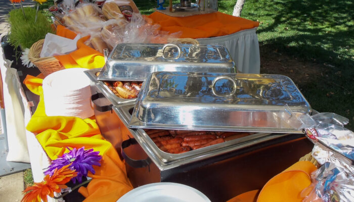 Freshly grilled hot dogs and bratwurst on a decorated buffet line at a company picnic produced by James Event Productions.
